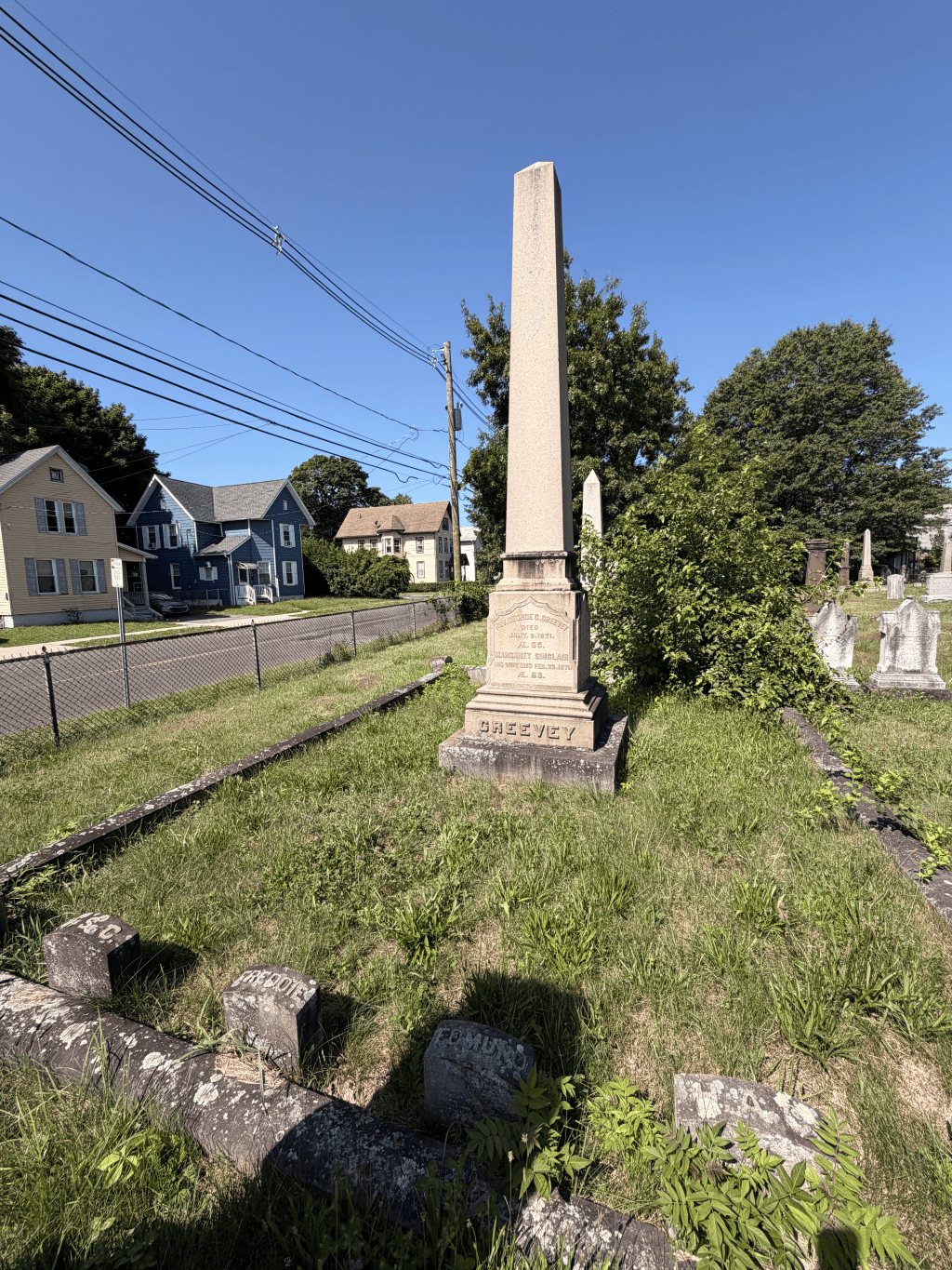 A tall pale stone obelisk stands within a bordered family plot at West Cemetery.